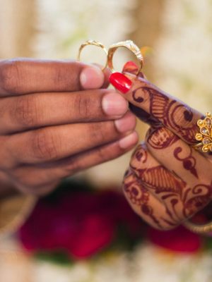 Close-up of hands with henna and jewelry during a traditional Indian wedding ceremony, exchanging rings.